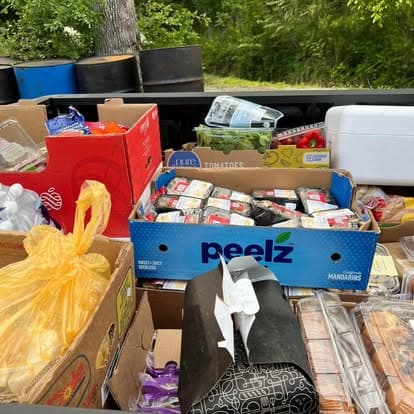 Boxes of groceries ready to hand out at Christ Family Church: fresh produce, packs of meat, tomatoes, bread and full yellow grocery bags.